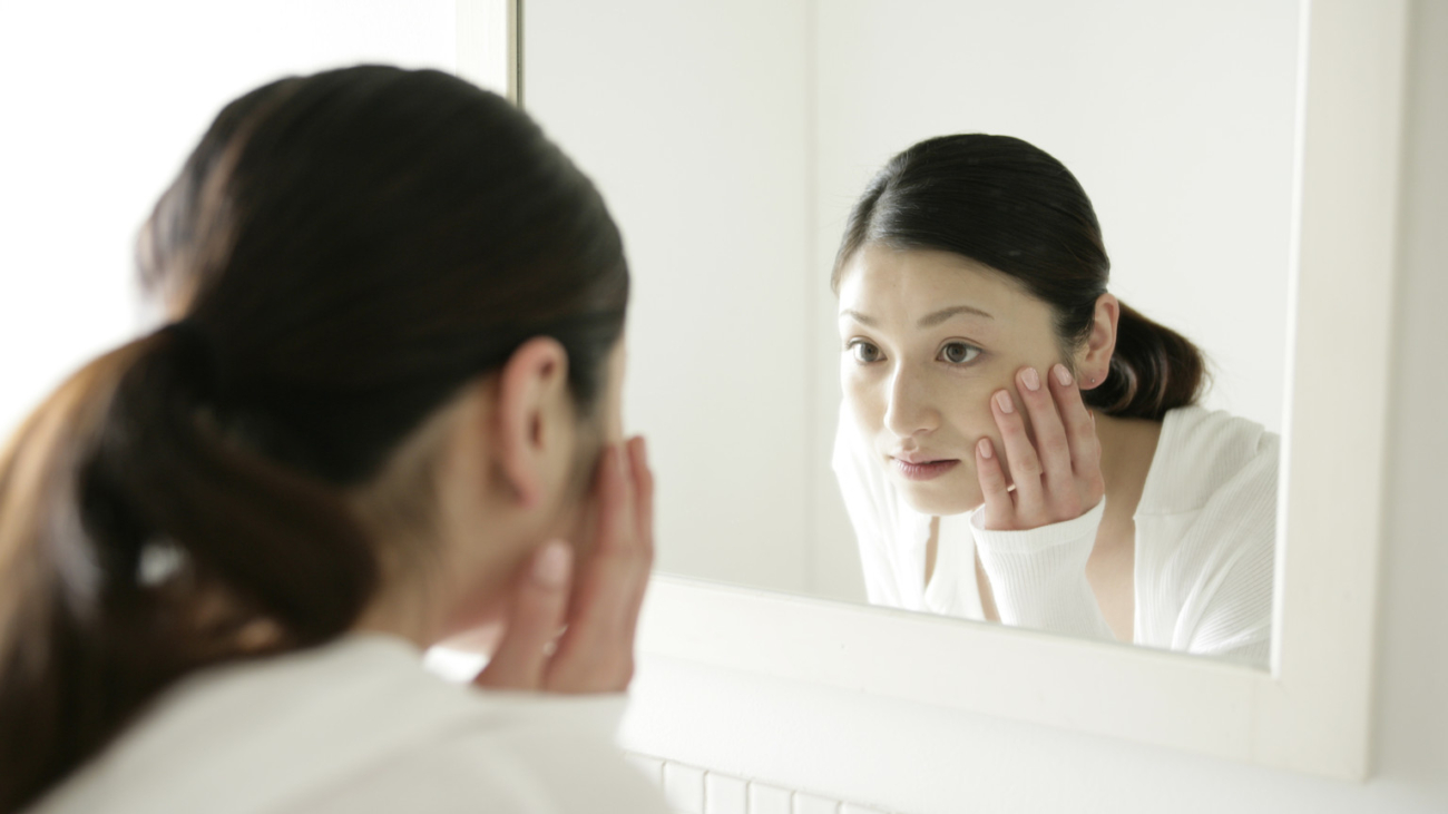 Close-up of a young woman looking into a mirror and touching her face