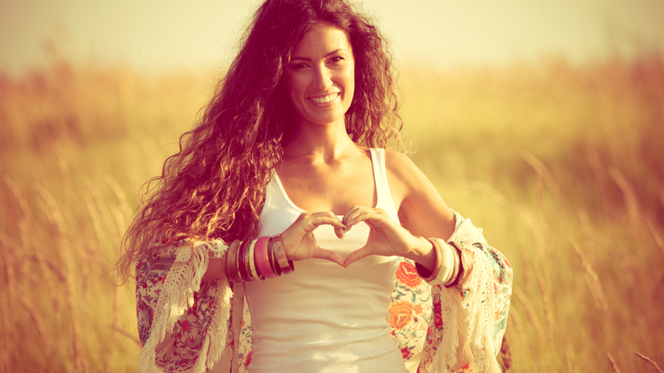 smiling young woman in summer field show heart shape hands sign